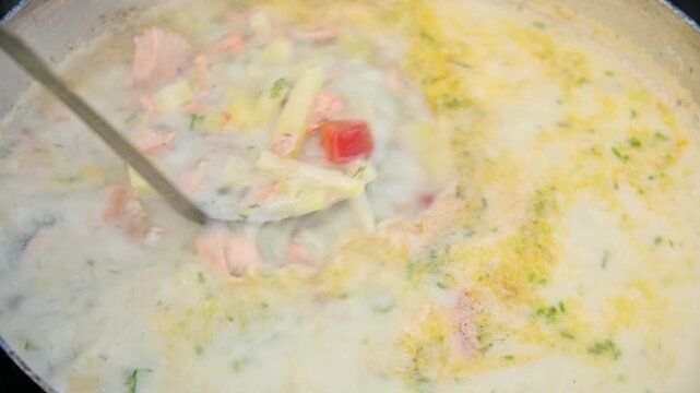 Stirring creamy fish soup in a metal pot