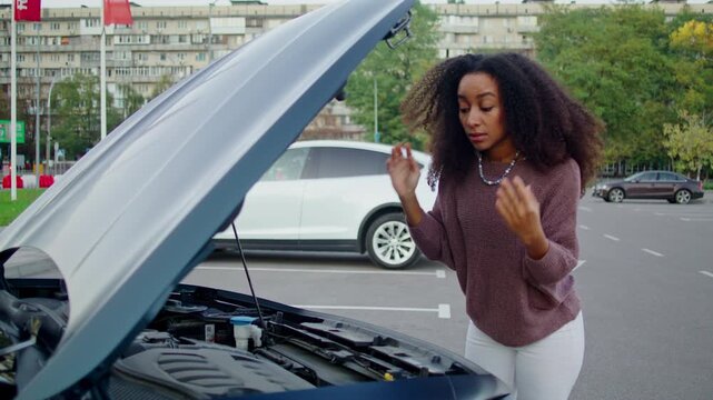 Woman driver carefully inspects engine beneath raised car hood