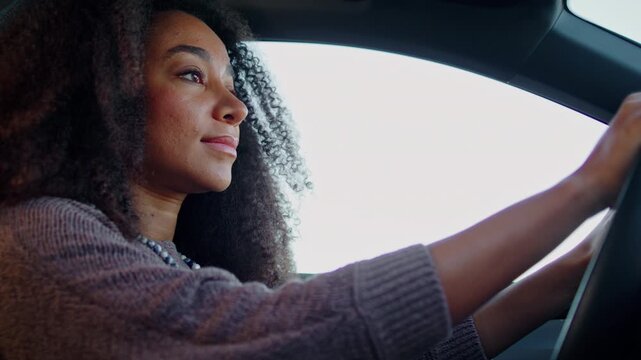 Woman driver with kinky hair steers automobile through streets