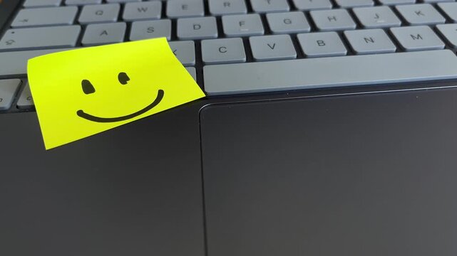 Smiley face sticky note on laptop keyboard and trackpad