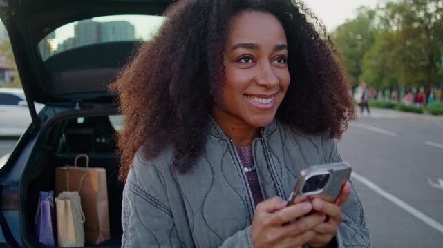 Smiling female driver stands near car on spacious parking area
