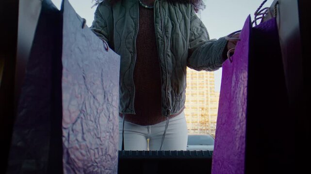 Woman arranges shopping bags in rear compartment of parked car