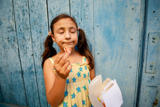 Child Enjoying Snack in Front of Blue Wooden Wall