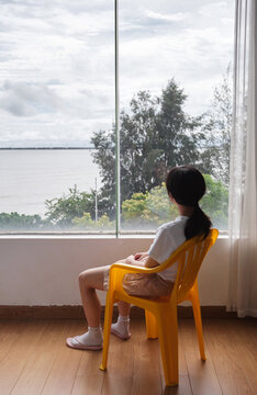 Chinese girl sits in front of a large window, looking out at the sea