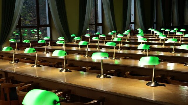 Empty historic library reading room with green banker lamps on wooden desks by autumn windows