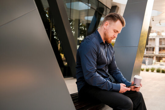 Portrait of groomed man holding smartphone and disposable cup outdoors