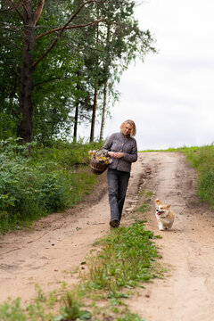 A woman and her corgi trot home along a rural dirt path