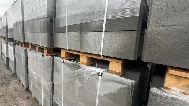 Stacked anPallets of grey concrete hollow masonry blocks wrapped and strapped in storaged wrapped concrete block pallets in outdoor storage. High quality 4k footage