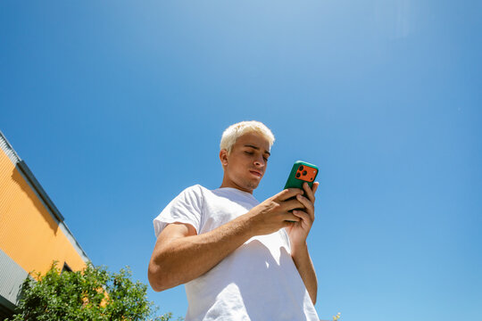 Young Man Looking at His Phone Under a Clear Blue Sky