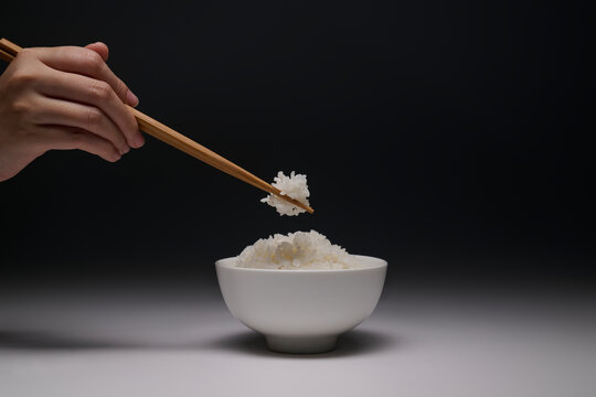 Hand using chopsticks to pick up a portion of white rice from a bowl