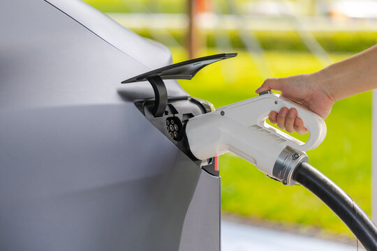 Hand plugging charging gun into electric car charging port