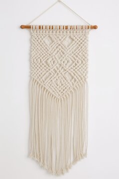 Handmade cream macrame wall hanging with a diamond weave pattern and long fringe, hanging from a wooden rod against a white background.