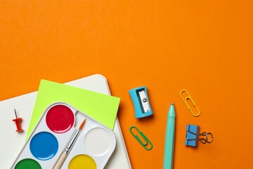 Top view of notebook and school stationery on orange background, copy space © Sunlight