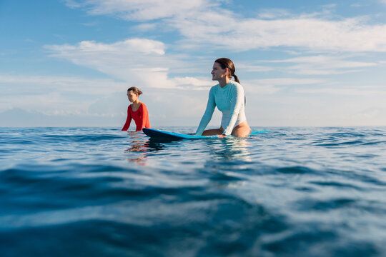 Couple of surfer women sitting on surfboards in sea and waiting for surfing waves