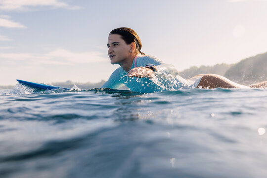 Surf girl rowing on surfboard. Woman in ocean during surfing