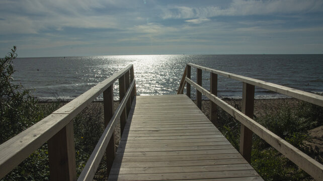 Scenic view of a wooden path down to the ocean beach under a blue sky with light clouds.