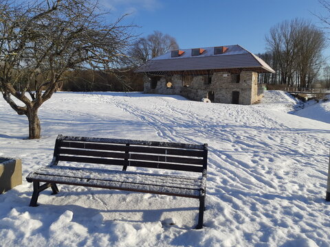 Old mild covered with snow with a bench in the foreground and tree without flower or leaves