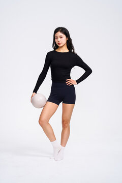 Fit Asian woman in black activewear holding pilates ball 