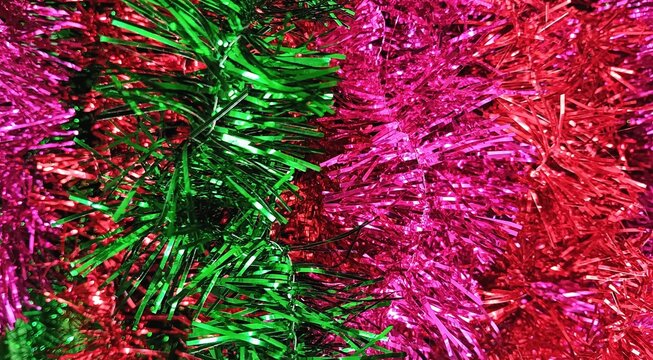 Vibrant Christmas tinsel decoration with green, pink and red metallic strands creating a colorful festive background for holiday designs.