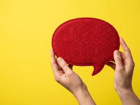 Two hands holding a red felt speech bubble on yellow background