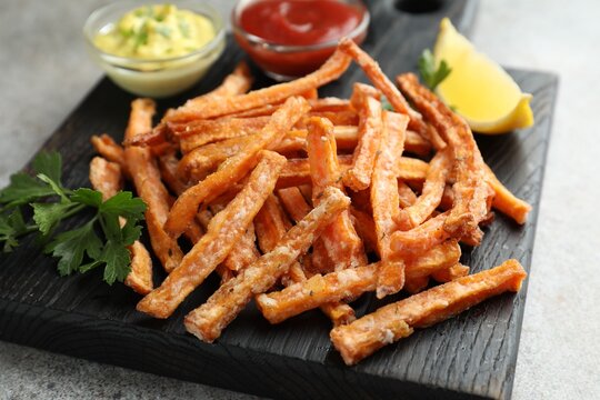 Sweet potato fries, sauces, lemon and parsley on grey table, closeup