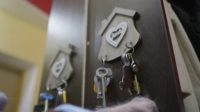 Person hangs a set of door keys on a wooden wall holder in the hallway. Warm interior lighting highlights the organized entryway setting as someone arrives back inside the house.