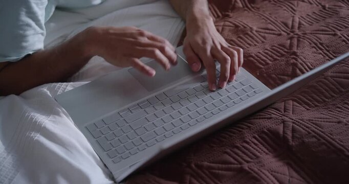 After settling on bed, hands are typing on silver laptop and using trackpad to work