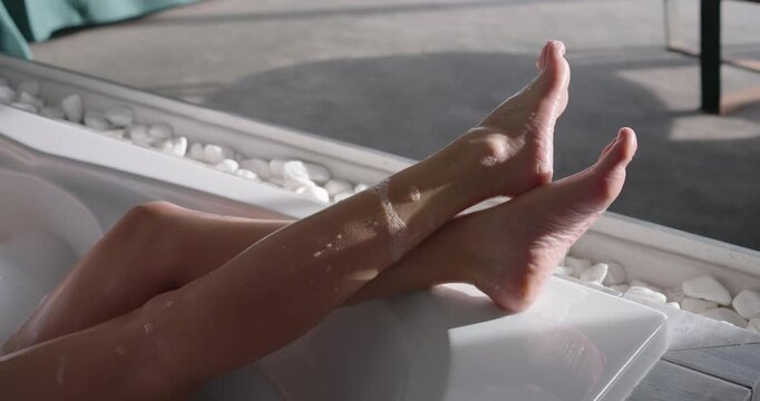Soap-coated legs and feet are flexing and shifting on tub ledge by glass door to rest