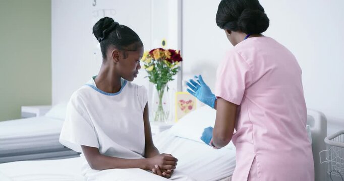 African American nurse in pink scrubs preparing and giving vaccine to teen on bed with syringe