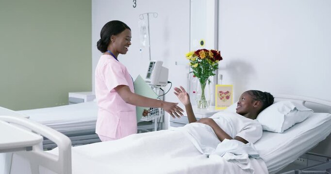 African American nurse in pink scrubs holding chart shaking reading calming child in hospital bed 3