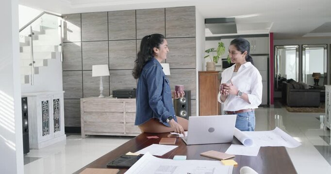 Indian women colleagues meeting at home workspace and reviewing laptop swatches mugs for review