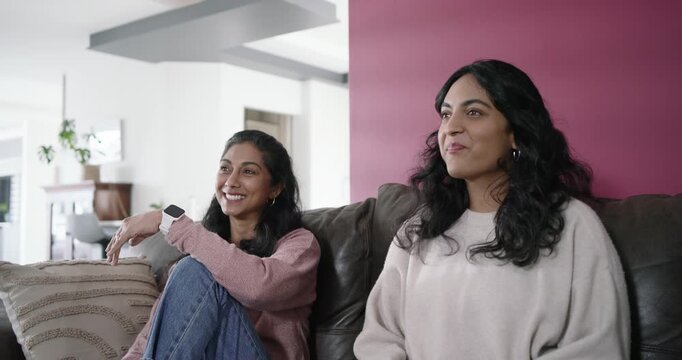 Indian female friends sitting on couch pointing laughing reaching into chip bowl reacting offscreen