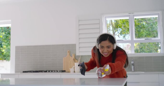 African American woman dancing to headset music while spraying kitchen island with sprayer