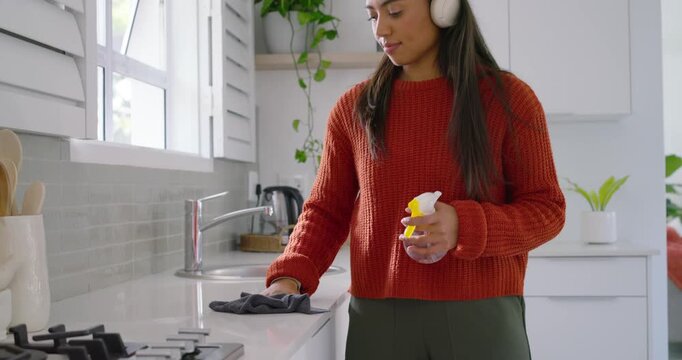 Adult woman with headphones, dancing to music, spraying and wiping kitchen with bottle and cloth