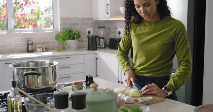 African American woman using knife chopping onion on island, checking pot for dinner, copy space