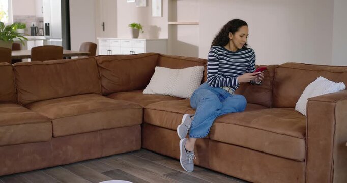 African American woman lifting feet to avoid approaching vacuum, using phone on couch, copy space