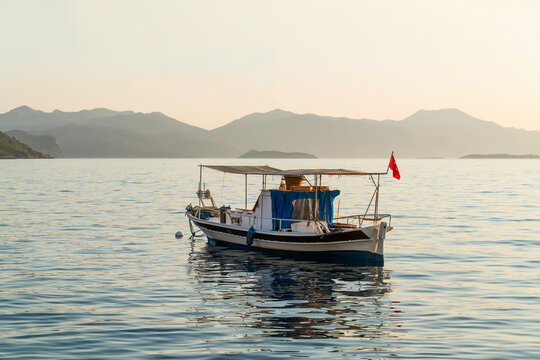 Seagull flying over a traditional fishing boat floating on calm sea at sunset in Sogut, Marmaris, Turkey