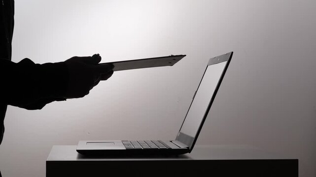 Person's silhouette holding a clipboard and pen, interacting with a laptop on a white background, representing data entry, digital information management, and modern workflow