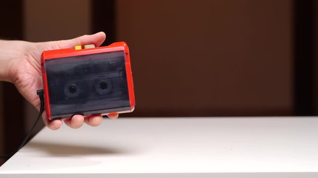 Hand holding red retro portable cassette player with visible tape inside, close up studio shot evoking 80s90s nostalgia for analog music technology and personal listening memories
