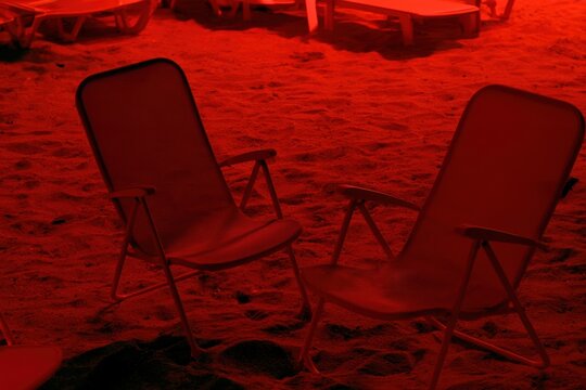 two empty beach chairs sit on a sandy surface under a dramatic red light