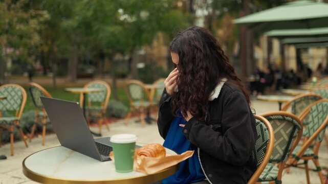 Coughing into white tissue at an outdoor cafe table today. Young woman with respiratory flu