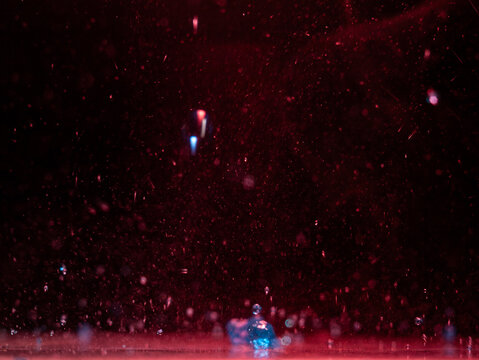 Water droplets and spray surround a person standing beneath red stage lights