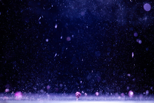 Water droplets fall onto a surface under blue and purple light