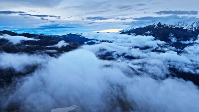 Dramatic wide shot reveals clouds rolling over dark mountain ridges during dusk near Mount Gongga in Sichuan, China.