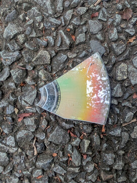 Broken optical disc fragment reflects rainbow colors on rough stone pavement