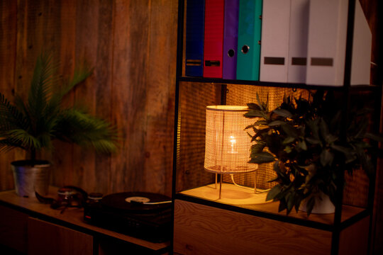 Soft lighting accentuates textured wall and stylish workspace environment. Gentle illumination from rattan lamp creates inviting atmosphere for home office or creative studio