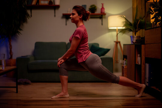 Individual engaged in stretching routine in comfortable living environment. Woman calmly practicing lunges in living space with soft lighting and relaxed atmosphere