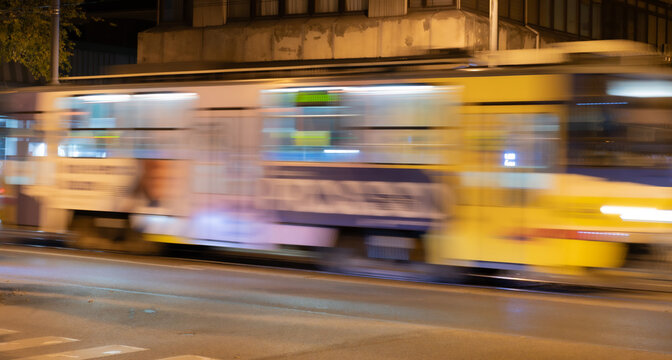 A moving yellow electric tram with light trails and motion blur effect driving through the illuminated city streets at night in Szeged, Hungary. Abstract urban public transportation long exposure phot