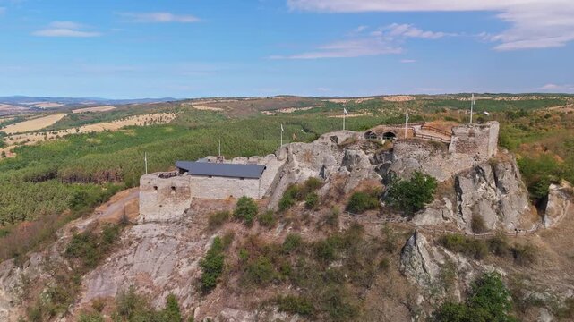 Aerial view of Sirok Castle, a medieval stone fortress on a rocky hilltop, overlooking forests, farmland and rolling hills near Sirok, Hungary, in summer.