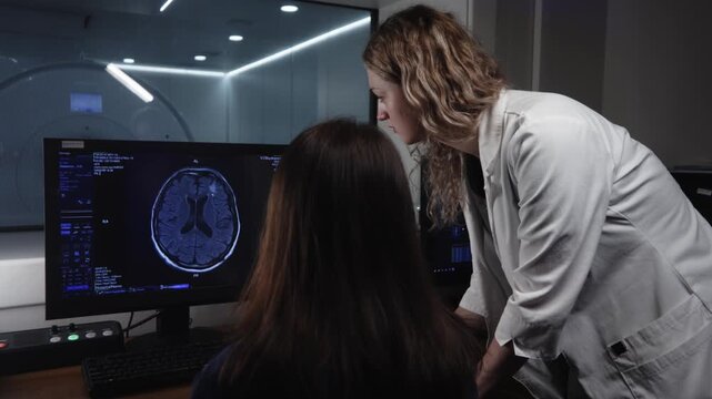 Radiologist reviewing brain MRI scan with patient beside imaging console in modern radiology control room